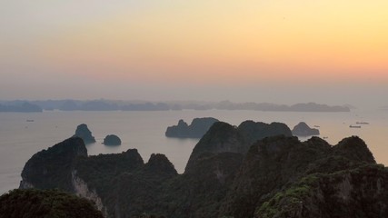 Aerial view on Halong bay during golden hour, with the iconic limestone karsts in the foreground and ships lying at anchor in the distance. A UNESCO world heritage site.