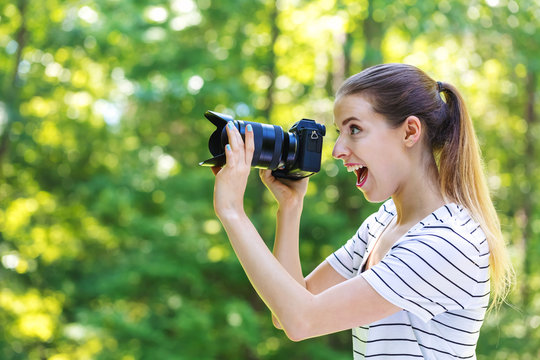 Young woman with a professional digital SLR camera on a bright summer day in the forest