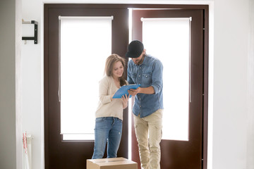 Female and male standing in hallway at home. Courier bring a cardboard box package. Customer signing receipt of the parcel. Surface mail, buy and order goods by post service by online internet concept