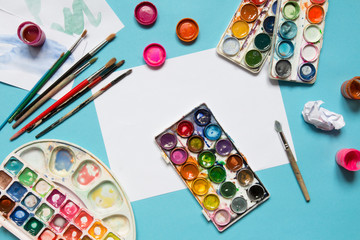 Set of artist accessories collection. Canvas, tube of oil paint, art brushes, palette knife lying on the blue table. Artist workshop background.