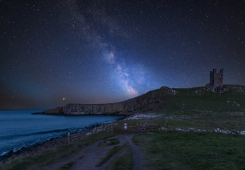 Vibrant Milky Way composite image over landscape of Dunstanburgh Castle on Northumberland coastline...