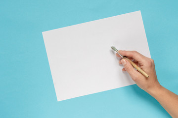 collection of accessories for artists. Canvas, oil paint tube, artistic brushes, palette, and hand with a brush lying on a blue table. Artist master background. Flat lay top view.