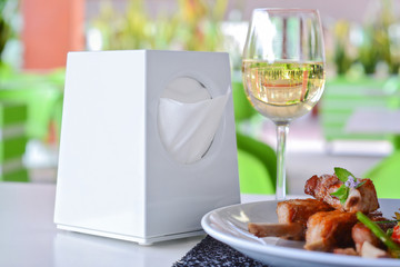 paper napkin holder for restaurant on served dinner table with grilled pork ribs and glass of white wine