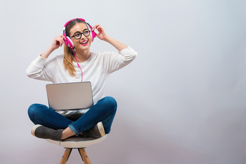 Young woman with headphones and her laptop on a gray background
