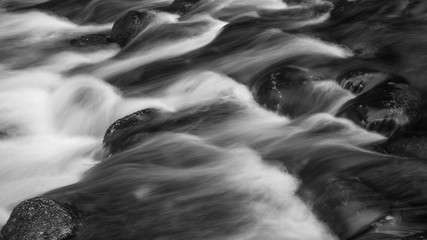 Detail intimate landscape image of river flowing over rocks with long exposure motion blur