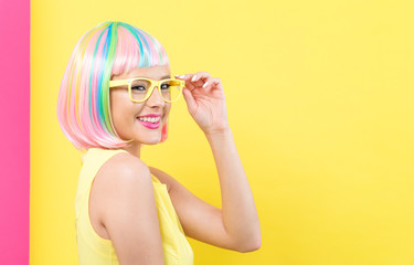 Young woman in a colorful wig with sunglasses on a split yellow and pink background