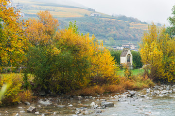 Picturesque autumnal view with a religious shrine by Isarco river. Foliage on the trees. Typical mountain scenery in winemaking region of Northern Italy, Europe. Novacella, Varna in South Tyrol. 
