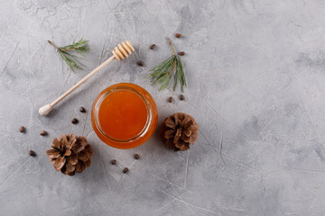 Fototapeta na wymiar Honey in a glass jar and honey stick. Set against colds with pine nuts conifer and pine cones.