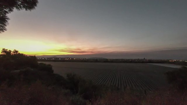 Sky over the parallel lines of the agriculture fields glows as sun peeks over distant mountain ridge horizon. 