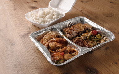 asian fast food from delivery service in a foil container and rice in a foam box on a wooden table, copy space