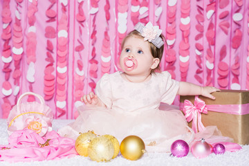 Baby girl with a Christmas balls in a festive pink interior