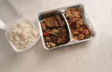 Asian fast food from delivery service in a foil container and rice in a foam box on a bright background, high angle view from above, copy space