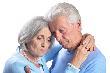 Portrait of sad senior couple hugging on white background