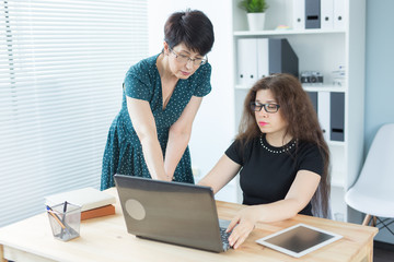Office, business people and graphic designer concept - Women sitting and discussing ideas at the office with laptop, looking at the screen, listening to opinions