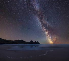 Vibrant Milky Way composite image over landscape of yellow sandy beach Three Cliffs bay
