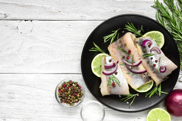 herring fillet with pepper, rosemary, onion and lemon on black plate on white background. top view...