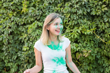 Holiday, holi and people concept - Beautiful young woman posing with green powder on her shirt