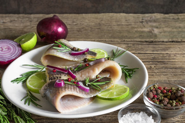 marinated herring fillet with pepper, rosemary, onion and lime in a plate on rustic wooden...