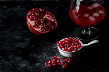 Tempting pomegranate, red seeds and fresh juice with the addition of ice on a black, stone background