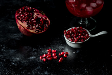 Tempting pomegranate, red seeds and fresh juice with the addition of ice on a black, stone background