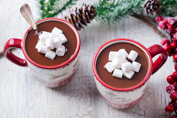 Hot chocolate with marshmallows in Christmas mugs on white cracked wooden background. Close up.
