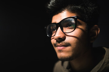 Hacker in glasses and a hood works at a computer in the dark, a reflection in glasses close-up.
