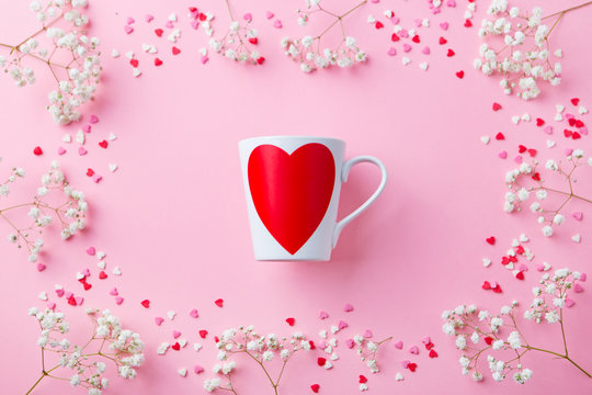 Romantic cup with white flowers and sugar colorful hearts. Pink pastel background. Top view. Copy space.