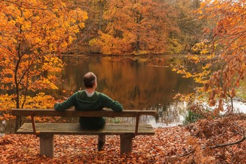 Mann sitzt auf einer Bank am Fluss in romantischer Herbst Landschaft, Konzept Auszeit, Balance,...