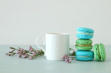 White vintage cup of coffee and colorful macaron or macaroon over pastel wooden table.