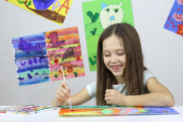 little girl draws a watercolor drawing on the background of a lot of drawings