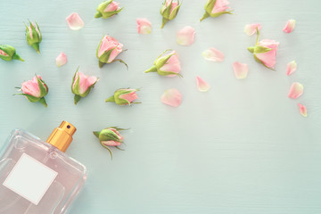 Top view image of perfume bottle with rose petals flowers over pastel blue background. Floral scent...