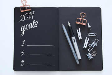 Top view 2019 goals list with notebook over wooden white desk.