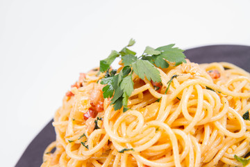 Spaghetti Carbonara with some parsley on a black plate on a white background