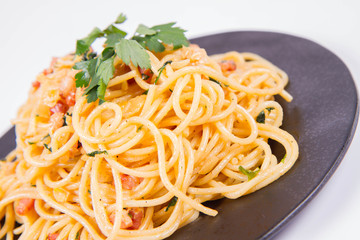 Spaghetti Carbonara with some parsley on a black plate on a white background