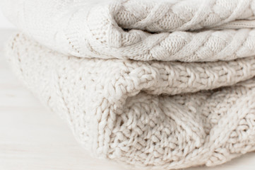 Two white knitted woolen sweaters pullover in a stack on wooden table on light background. Fashion Clothes Trendy Cozy Jumper. Autumn and winter clothes, space for text