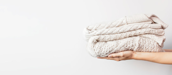 Two white knitted woolen sweaters pullover in a stack in female hands on light background. Fashion Clothes Trendy Cozy Jumper. Autumn and winter clothes, space for text