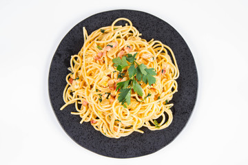 Spaghetti Carbonara with some parsley on a black plate on a white background