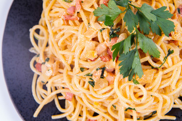 Spaghetti Carbonara with some parsley on a black plate on a white background