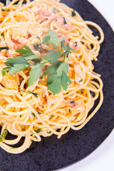 Spaghetti Carbonara with some parsley on a black plate on a white background