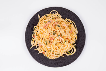 Spaghetti Carbonara with some parsley on a black plate on a white background