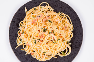 Spaghetti Carbonara with some parsley on a black plate on a white background