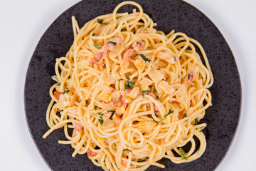 Spaghetti Carbonara with some parsley on a black plate on a white background