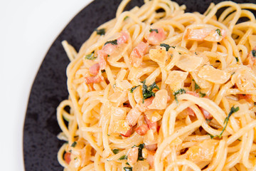 Spaghetti Carbonara with some parsley on a black plate on a white background
