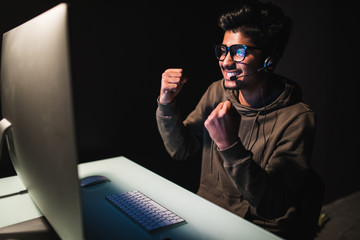 Ecstatic asian gamer boy rejoicing victory while playing video games on computer in dark room...