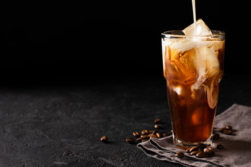 tall glass cold brew coffee with ice and milk on black or dark background