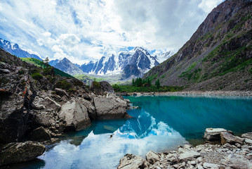 Mountain lake is surrounded by large stones and boulders on front of giant beautiful glacier. Amazing snowy mountains. Ridge with snow. Wonderful atmospheric landscape of majestic nature of highlands.