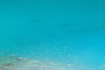Amazing textured background of calm azure clean water surface. Sunshine in mountain lake close up. Beautiful ripples on shiny water in sunny day. Wonderful relax texture.
