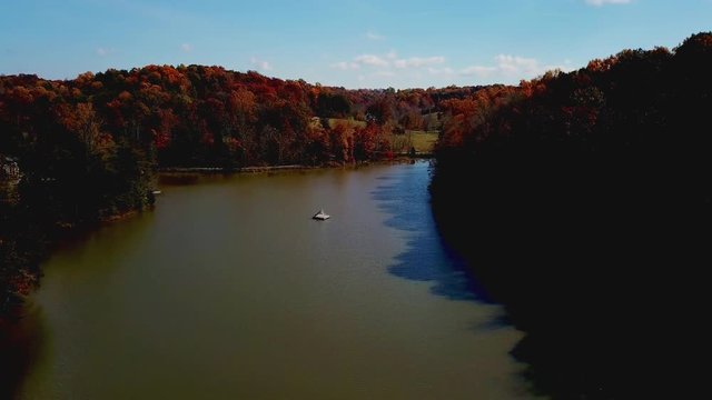 Flying above rural lake with beautiful autumn treetops and stunning lush autumn foliage comes into view. Aerial view. Red fall colors.