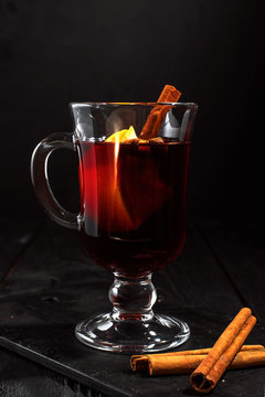 closeup glass of mulled wine with orange and cinnamon on dark black background