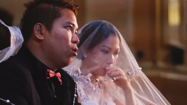 Bride and Groom chat as they Listen to Mass during Catholic wedding at the church